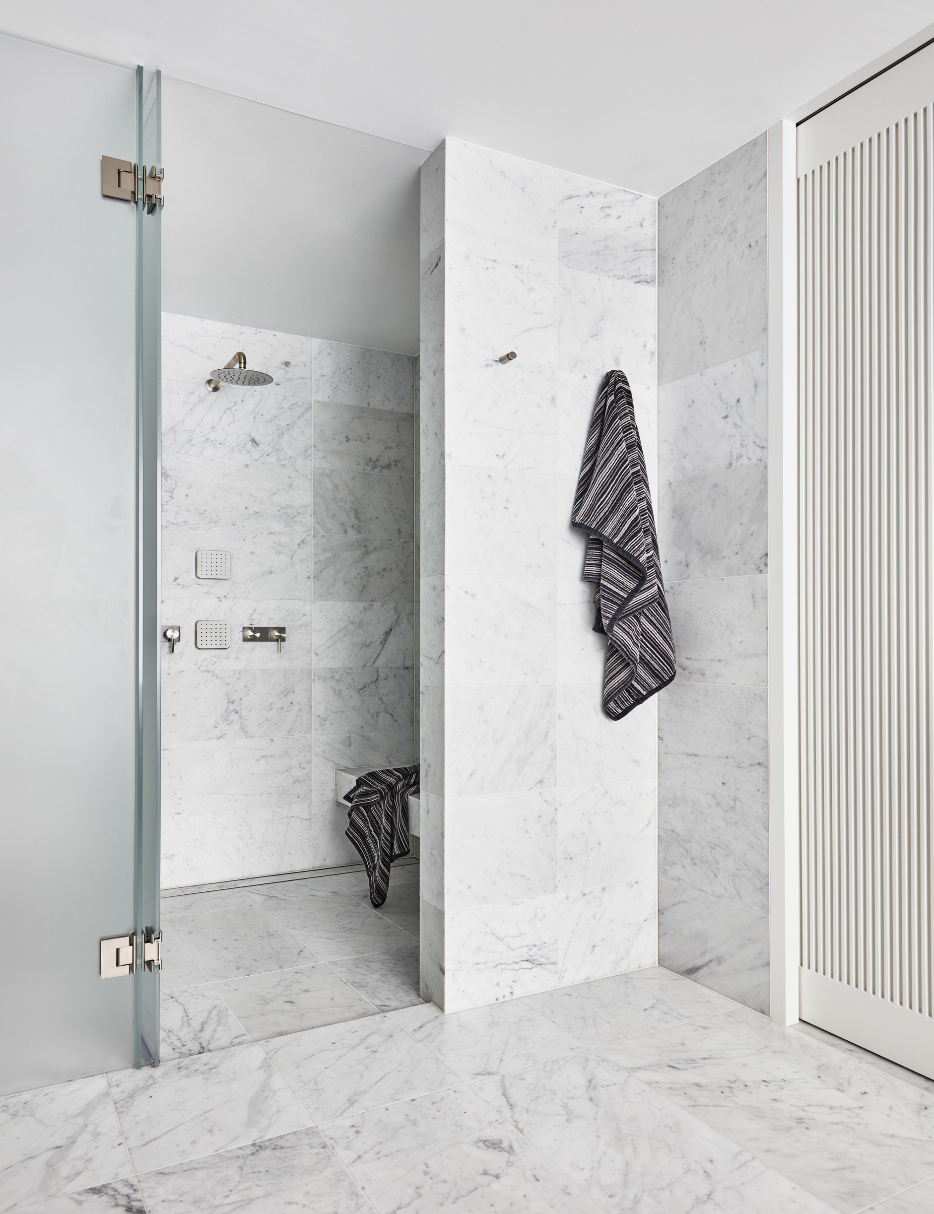 White marble bathroom renovation with marble shower seat and sliding doors by Sydney interior designers, Brendan Wong Design