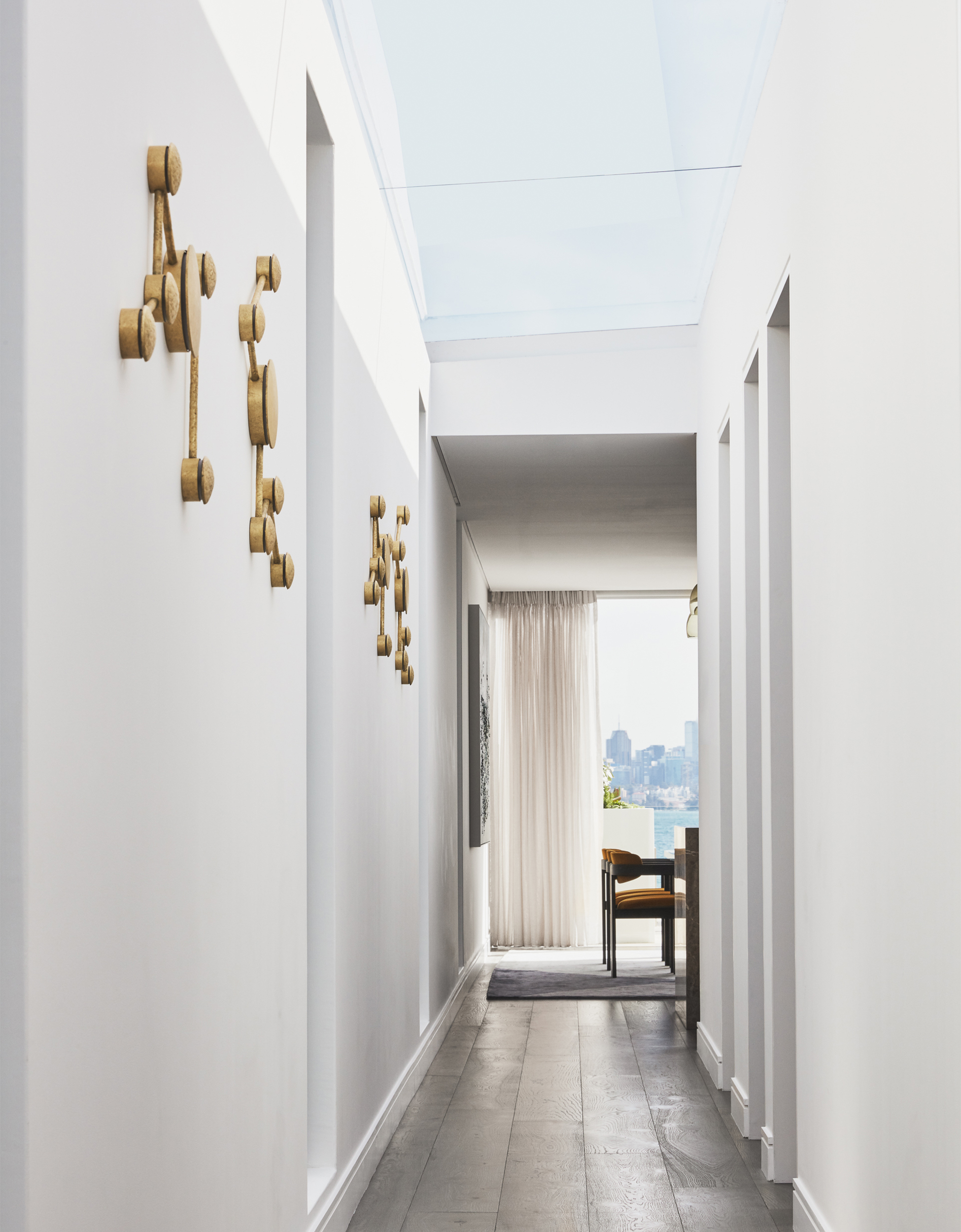 White hallway in coastal apartment with skylight windows and Porta Romana wall lights by Sydney interior designers