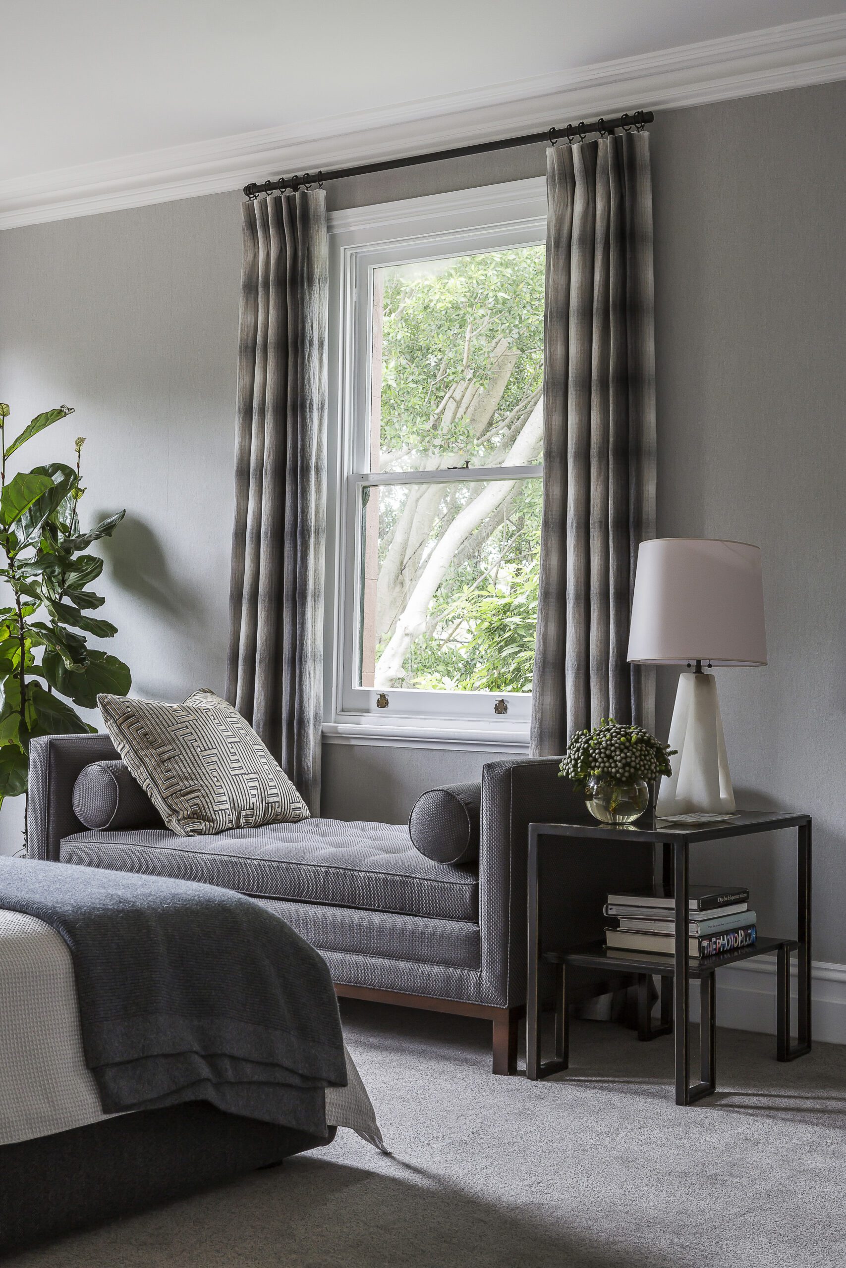 Calm and contemporary bedroom with soft grey tones, tailored chaise lounge, and leafy garden views, designed by Brendan Wong Design at East House.