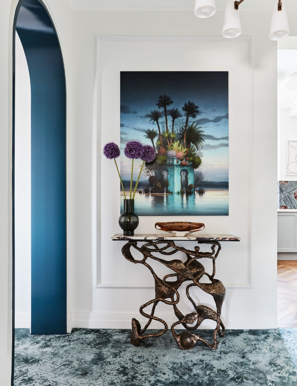 Hallway adorned with contemporary Alexander McKenzie artwork, a glossy hallway arch, bronzed kelp console, and strategic lighting, exemplifying Brendan Wong Design's attention to detail.